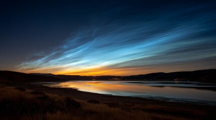 Fototapeta premium A tranquil lake reflects a vibrant twilight sky filled with deep blue and golden hues, while thin clouds gently float above the serene water