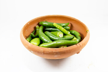 A collection of fresh green chilies displayed in a handmade clay bowl on white background