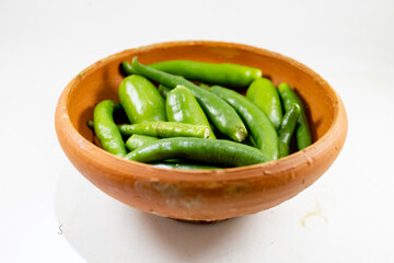 A collection of fresh green chilies displayed in a handmade clay bowl on white background