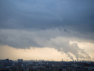 Panoramic view of a city with numerous residential buildings and an industrial area in the background. Factories emit thick smoke into the sky, causing severe air pollution