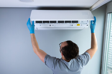 Technician Performing Maintenance on an Air Conditioning Unit While Wearing Protective Gloves in a...