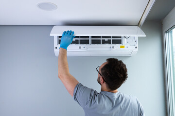 A Skilled Technician Performing Maintenance on a Ceiling-Mounted Air Conditioning Unit with Focus...