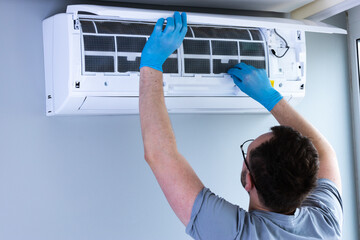 Man in Grey Shirt and Blue Gloves Performing Maintenance on Air Conditioning Unit in Modern...