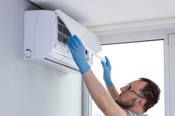 A Technician Performing Maintenance on a Wall-Mounted Air Conditioner Unit in a Bright Room with...