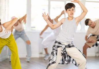 Happy teenage boy practicing basic hip-hop moves in training hall during group dancing classes