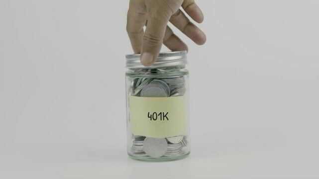 401k text or word on yellow sticky notes attached to a coin jar, hand inserting a coin before sealing the lid, white background