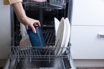 A Close-Up View of a Hand Reaching into a Dishwasher to Remove a Blue Textured Container Alongside Various Plates and Dishes Inside the Appliance