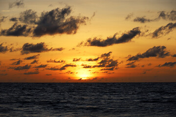 Fototapeta premium Sunset on a beach, orange sun is shining through the dark clouds. Sea background for romantic travel