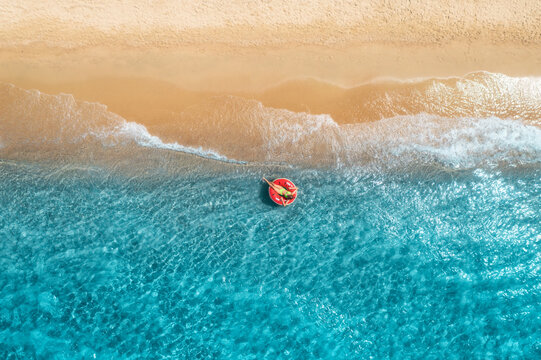 Aerial view of a woman swimming with red swim ring in blue sea at sunset in summer. Tropical landscape with girl, clear water, waves, sandy beach. Top drone view. Vacation. Sardinia island, Italy