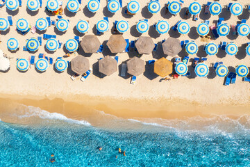 Aerial view of colorful umbrellas on white sandy beach, swimming people in blue sea at sunset in...
