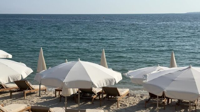 Sunny beach with white umbrellas and wooden lounge chairs facing the calm blue sea. Luxury seaside resort, perfect summer escape, travel destination background