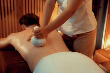 Hot herbal ball spa massage body treatment, masseur gently compresses herb bag on man body....