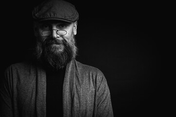 Black and white, portrait of an emotional bearded man in a gray hat, gray sweater and glasses...