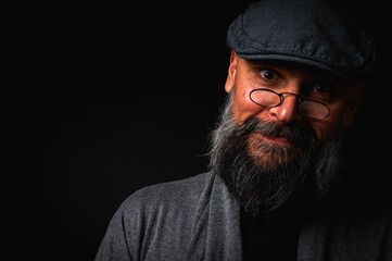 Portrait of an emotional bearded man in a gray hat, gray sweater and glasses looking at the camera...