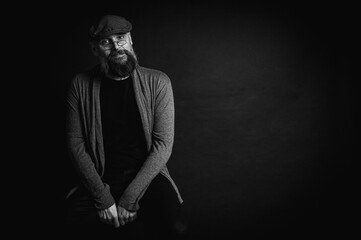 Black and white, portrait of an emotional bearded man in a gray hat, gray sweater and glasses...