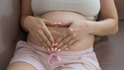 Pregnant woman holds her hands in a heart shape on her belly. 