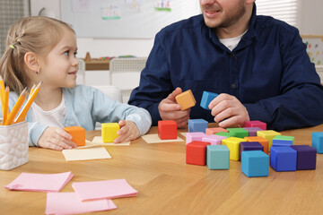 Teacher and little girl with colorful cubes at desk indoors, closeup