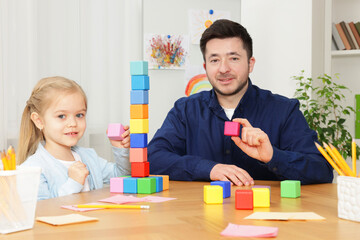Teacher and little girl with colorful cubes at desk indoors