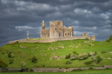 A breathtaking view of magnificent ancient Rock of Cashel ruins, majestically perched on a lush green hillside, enveloped by moody and dramatic clouds ideal for historical themes, Tipperary, Ireland
