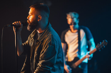 Singer performing live with guitarist in background on dark stage