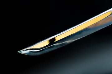 Extreme close-up of a polished katana tip with visible hamon and golden reflection, set against a...