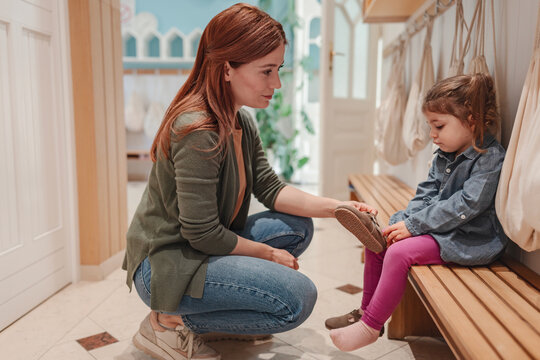 Preschool teacher kneels to talk kindly with a young girl in the changing area, offering comfort and support in a warm, nurturing early childhood setting.