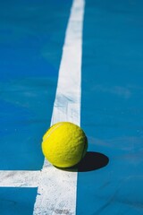 Pelota de tenis amarilla sobre cancha azul con líneas blancas bajo luz solar