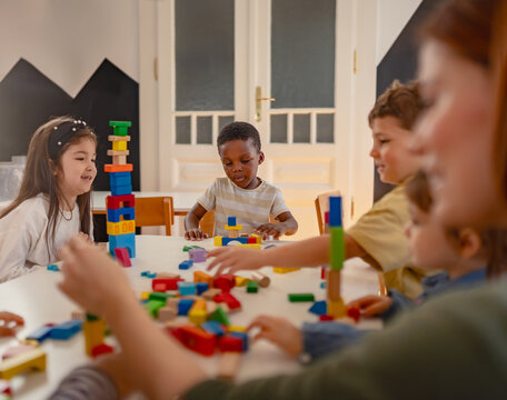 A teacher and diverse group of children build with colorful blocks in a classroom, promoting teamwork, creativity, and multicultural early learning.