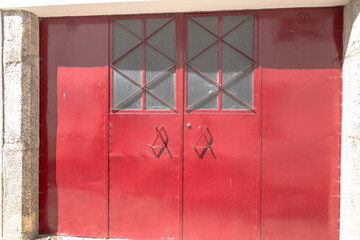 Bright daylight photo of a large red metal garage door with decorative window grids and stone...