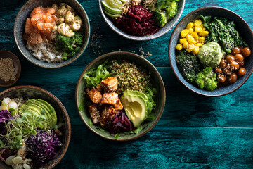 Overhead shot of five bowls filled with colorful, healthy ingredients like salmon, avocado, quinoa, and vegetables, showcasing a variety of nutritious and delicious meal options