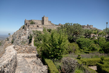 Obraz premium The medieval castle of Marvão, Portugal, stands atop a rocky cliff surrounded by gardens and ancient walls. Photographed on a clear summer day, this national monument overlooks the Alentejo plains.
