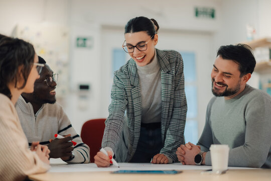 Smiling businesswoman drawing on blueprint during office meeting