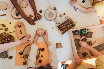 Multicultural preschool children engage in a nature-inspired craft activity with teachers, using wood slices and acorns in a warm, hands-on learning classroom.