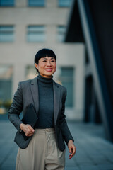 Smiling businesswoman walking outside office holding tablet looking away