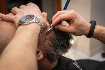Close-up of a barber trimming a beard with electric clippers in a modern barbershop. Professional men's grooming and beard care service, selective focus