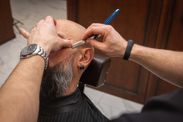 Close-up of a barber trimming a beard with electric clippers in a modern barbershop. Professional men's grooming and beard care service, selective focus