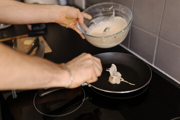 A close-up shot of a man pouring pancake batter mix into a hot frying pan, soft focus