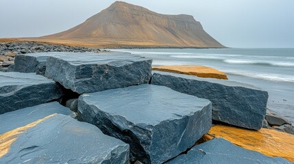 Coastal rocks and a mountain backdrop.  Large, dark gray rectangular stones form a  protective barrier on 