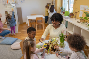 Teacher and curious children explore soil and plants in a classroom science activity, encouraging hands-on learning and environmental awareness in a diverse group of students.