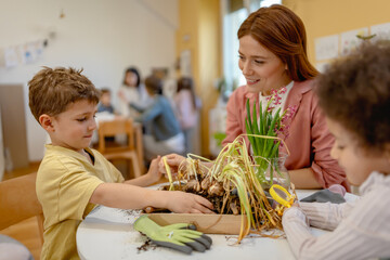 Teacher and curious children explore soil and plants in a classroom science activity, encouraging...