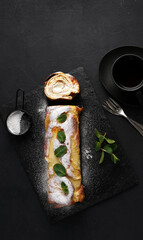 Finnish pancake pannukakku rolled up and filled with cream on a black board on a black background with cup of tea. tasty breakfast, top vertical view, copy space