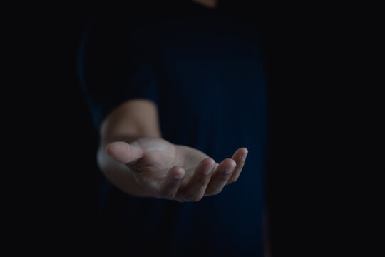 Person is standing and show an outstretched hand with an open palm. Business man showing empty hand and presenting isolated on black background. Hold, give, receive, help, gesture, present concept. - Powered by Adobe