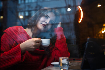 Reflection of a young woman drinking coffee in a cafe