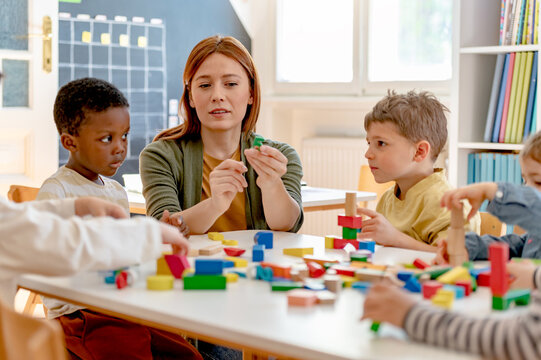 A teacher and diverse group of children build with colorful blocks in a classroom, promoting teamwork, creativity, and multicultural early learning.