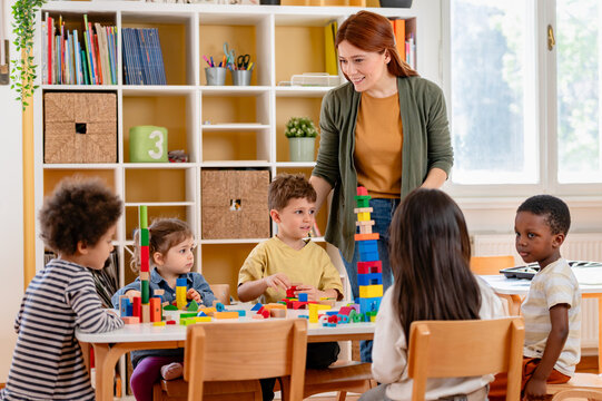 A teacher and diverse group of children build with colorful blocks in a classroom, promoting teamwork, creativity, and multicultural early learning