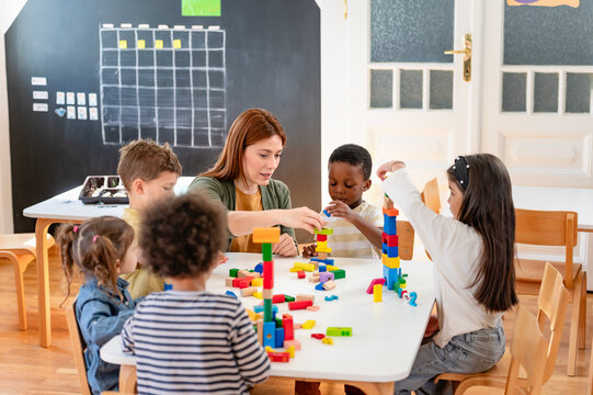 A teacher and diverse group of children build with colorful blocks in a classroom, promoting teamwork, creativity, and multicultural early learning.