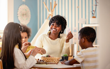 Preschool teacher guides a diverse group of children in a natural materials activity, encouraging...