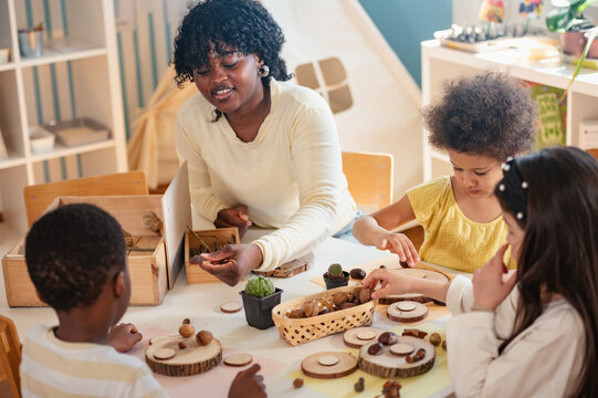 Preschool teacher guides a diverse group of children in a natural materials activity in a bright, creative classroom setting focused on hands-on learning.
