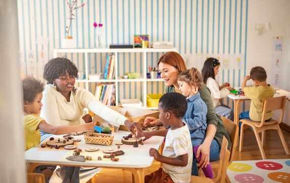 Diverse group of preschool children engage in a nature-based learning activity with two teachers, using wood and natural objects to explore creativity and tactile skills in the classroom.