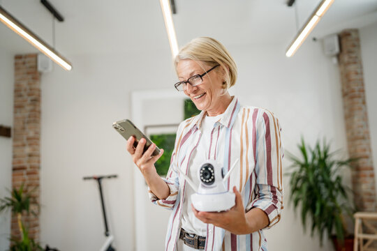 woman mature caucasian hold adjust home security camera and smartphone